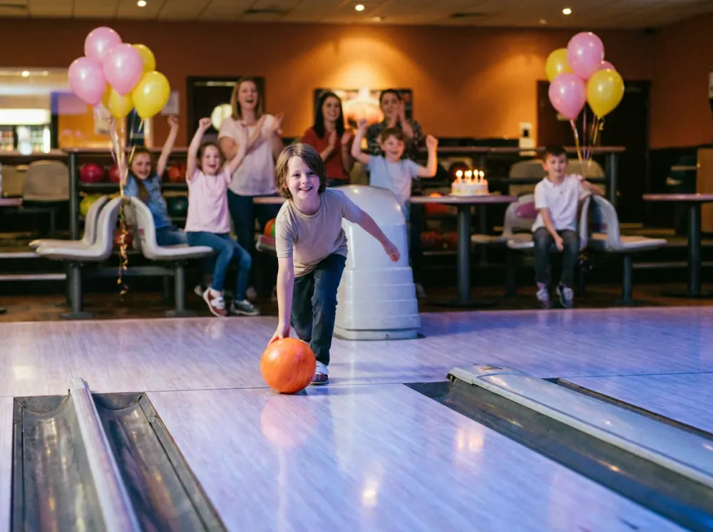 A child bowling at a birthday party while friends cheer
