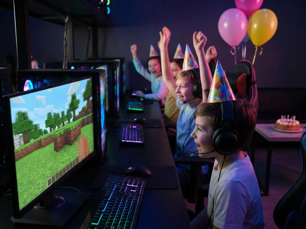Kids in party hats cheering at gaming computers with Minecraft on the screen